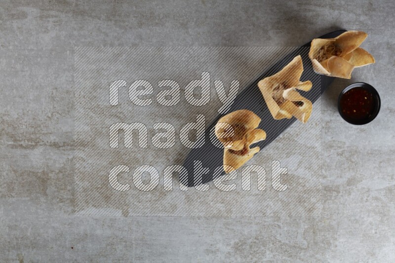 wonton cups with soy sauce ramkin on oval slate on grey textured counter top