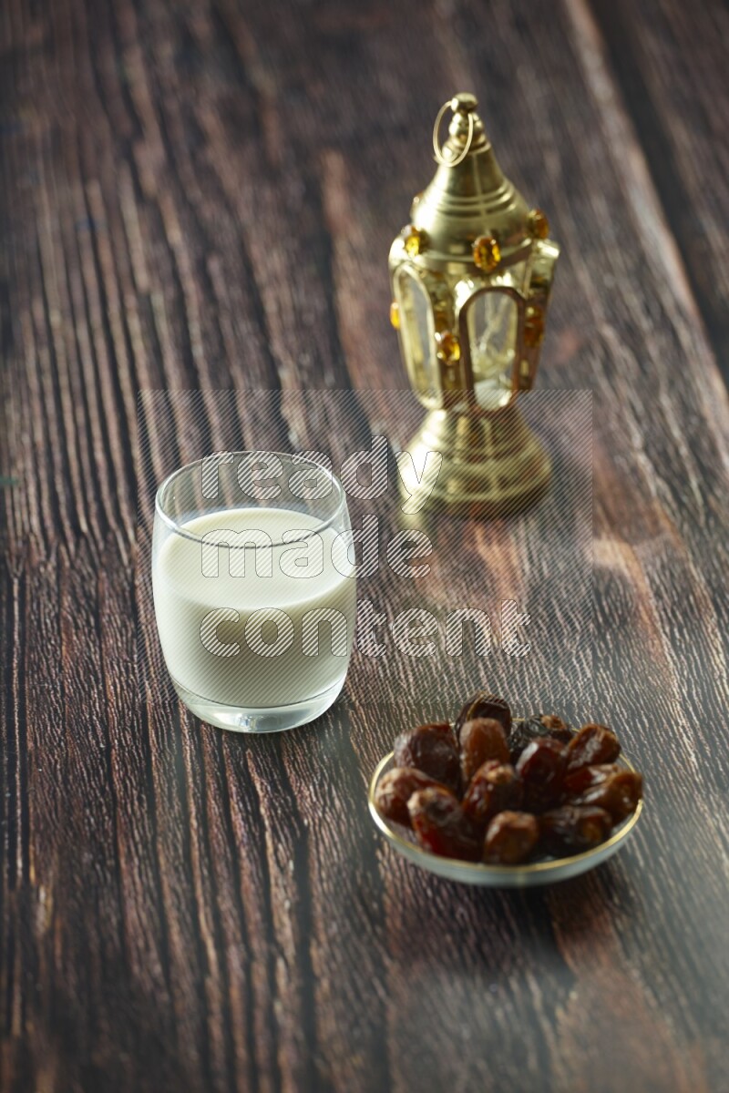 A golden lantern with different drinks, dates, nuts, prayer beads and quran on brown wooden background