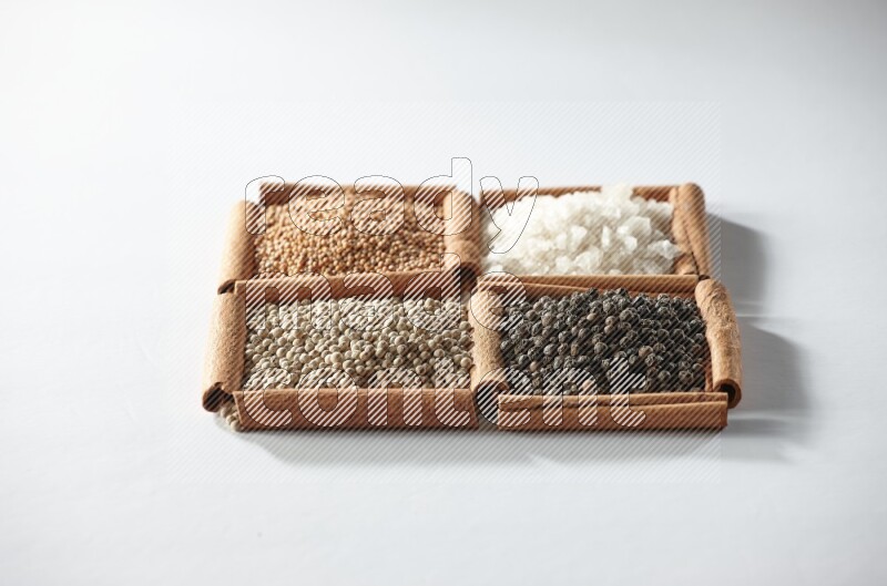 4 مربعات من أعواد القرفة ممتلئة بالخردل والملح والفلفل الأبيض والفلفل الأسود على أرضية بيضاء