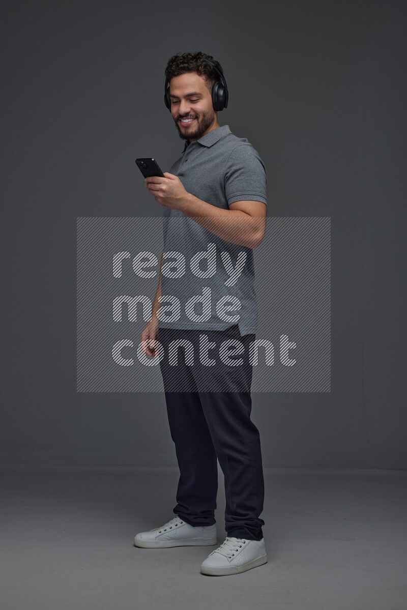 A man wearing casual and using his phone and headphone eye level on a gray background