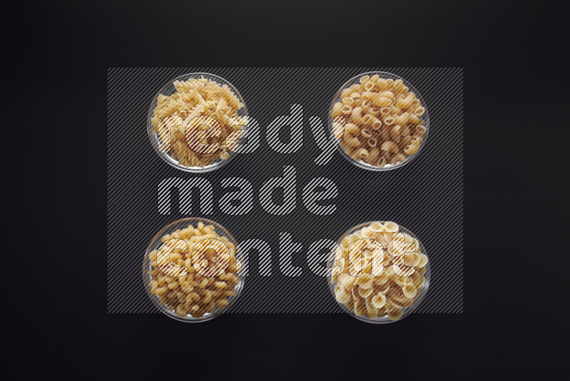 Different pasta types in glass bowls on black background