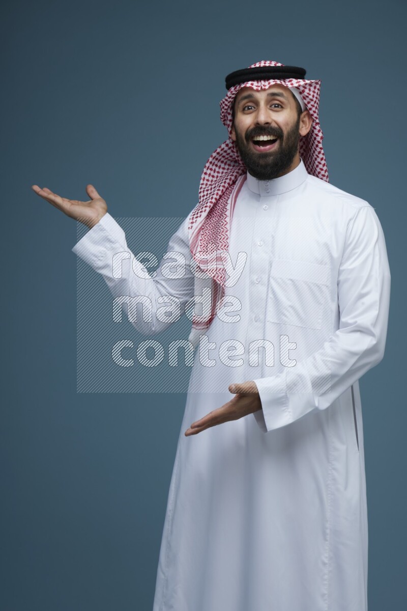 A man pointing in a blue background wearing Saudi Thob and Shomag