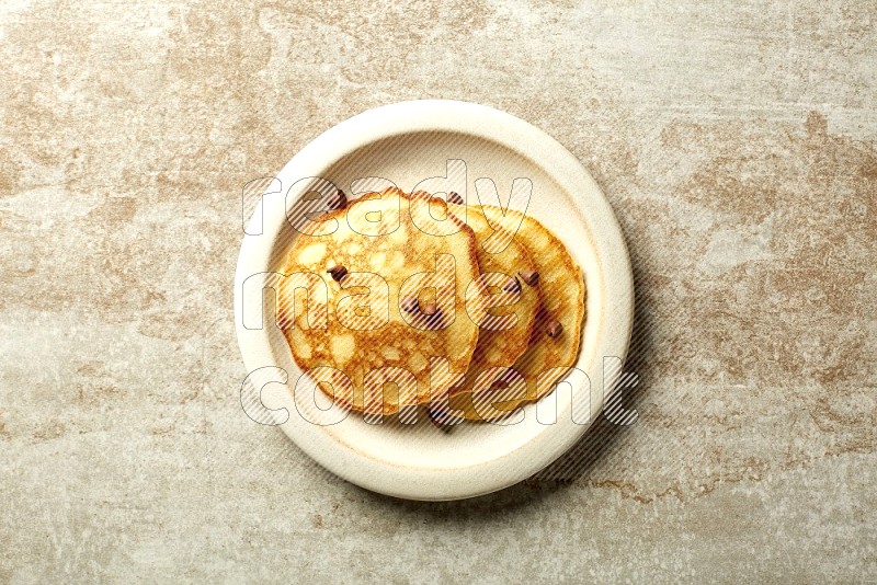 Three stacked chocolate chips pancakes in a beige plate on beige background