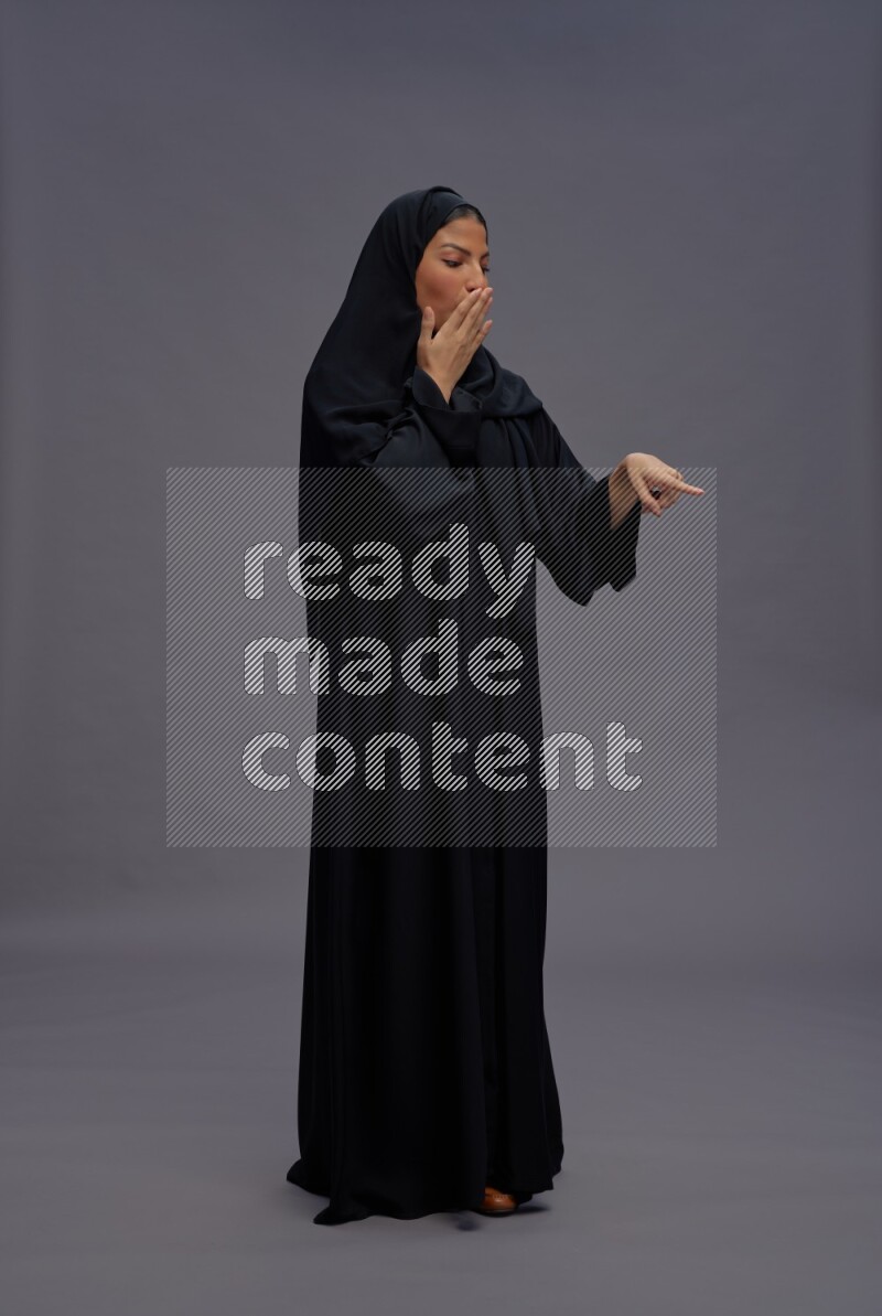 Saudi woman wearing Abaya standing interacting with the camera on gray background