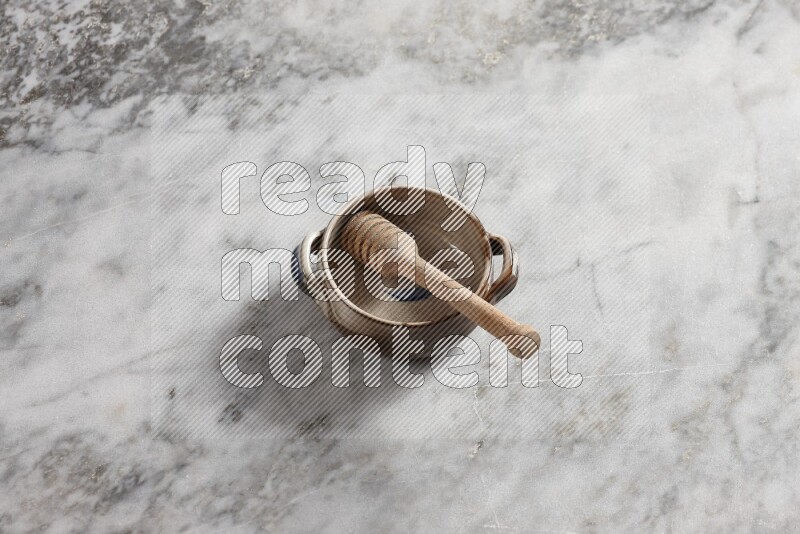 Multicolored pottery bowl with wooden honey dipper in it on grey marble background