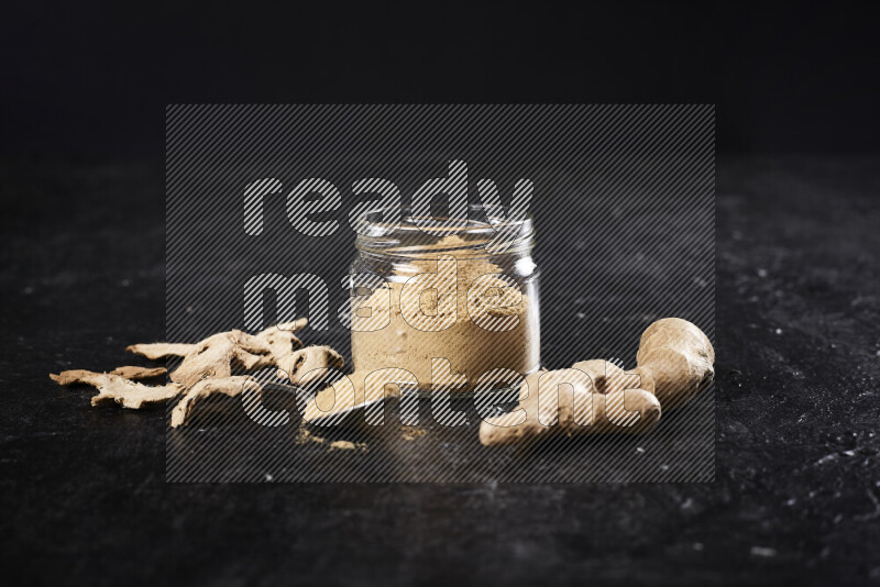 A glass jar full of ground ginger powder on black background
