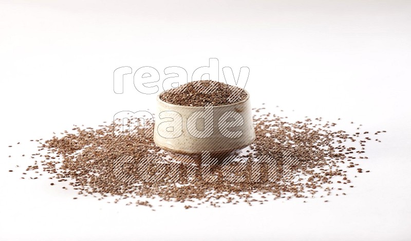 A pottery beige bowl full of flax seeds and more seeds spread on a white flooring