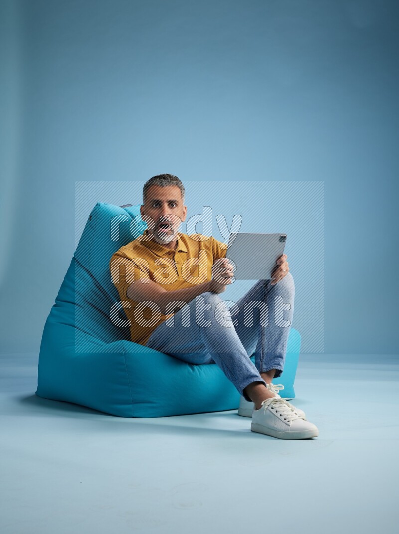 A man sitting on a blue beanbag and working on tablet