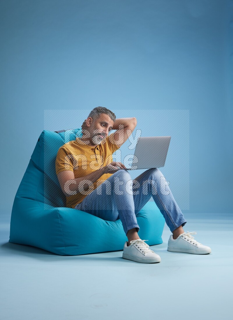 A man sitting on a blue beanbag and working on laptop