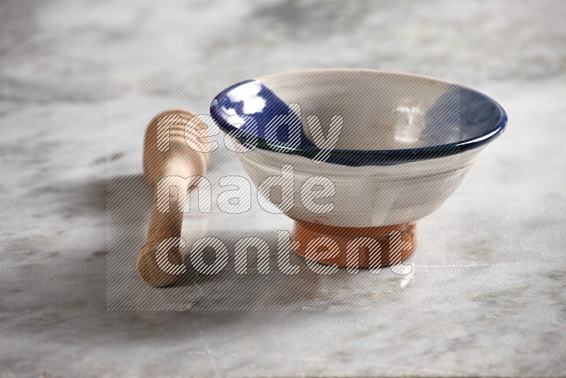 Multicolored Pottery bowl with wooden honey handle on the side with grey marble flooring, 15 degree angle