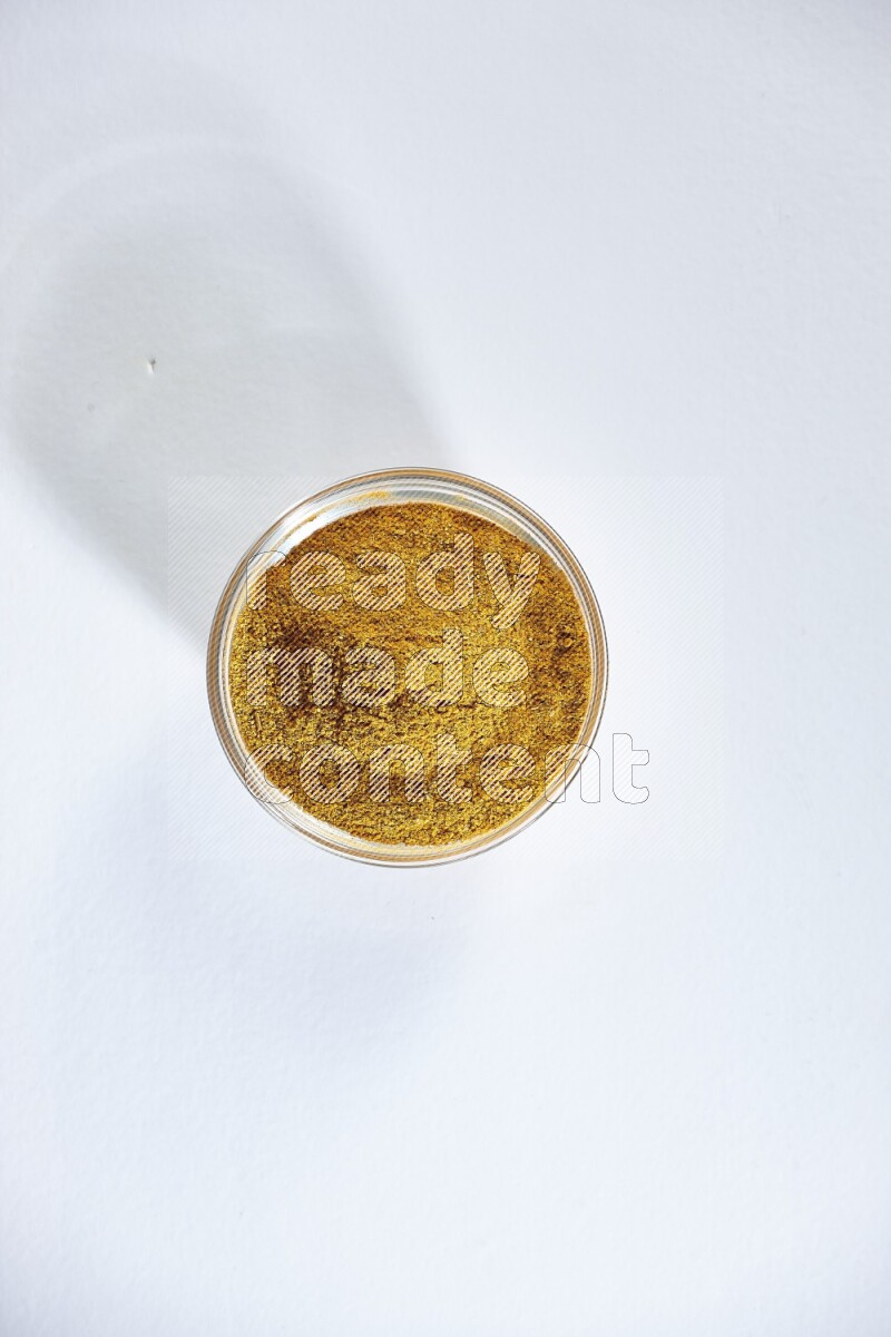 A glass bowl full of turmeric powder on white flooring