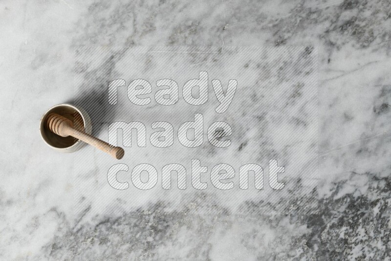 وعاء فخاري أسود مع ملعقة عسل خشبية بداخله على خلفية من الرخام الرمادي