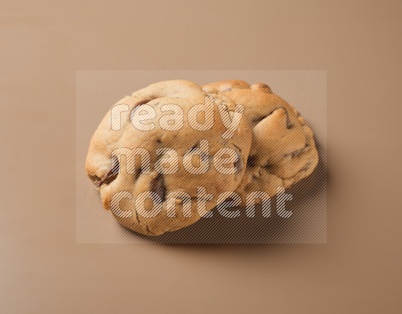 Two chocolate chip cookies on a brown background