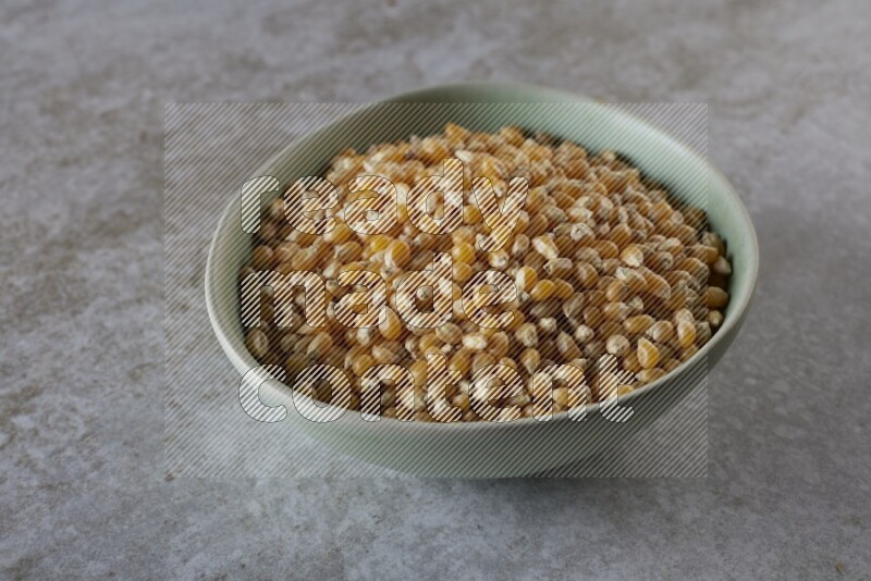 corn kernel in a green ceramic bowl on a grey textured countertop
