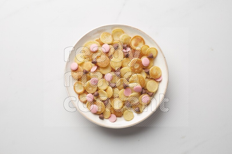 Top-view shot of mixed chocolate chips cereal pancakes in a round bowl on white background