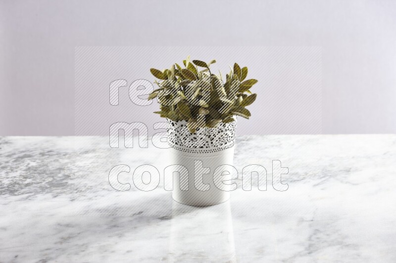 Green artificial plant in white decorative pot on grey marble background