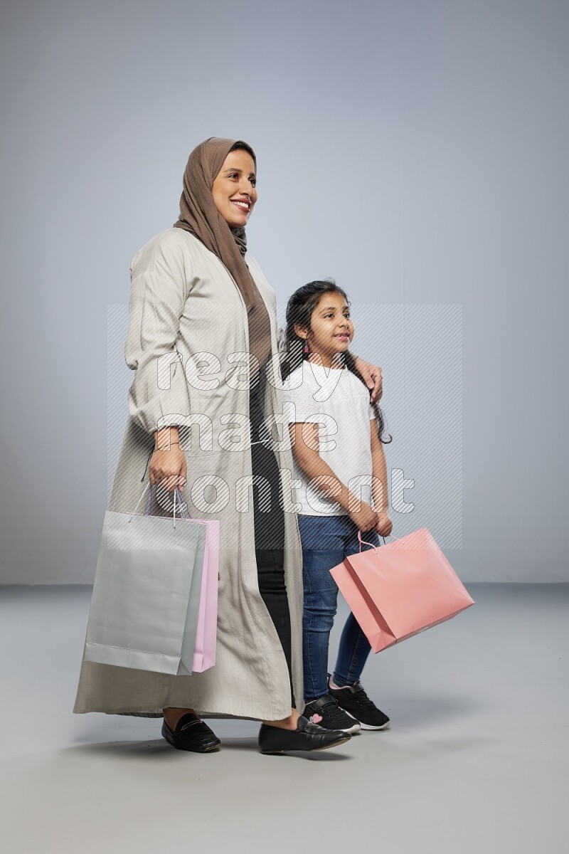 Mom and daughter holding shopping bags on gray background