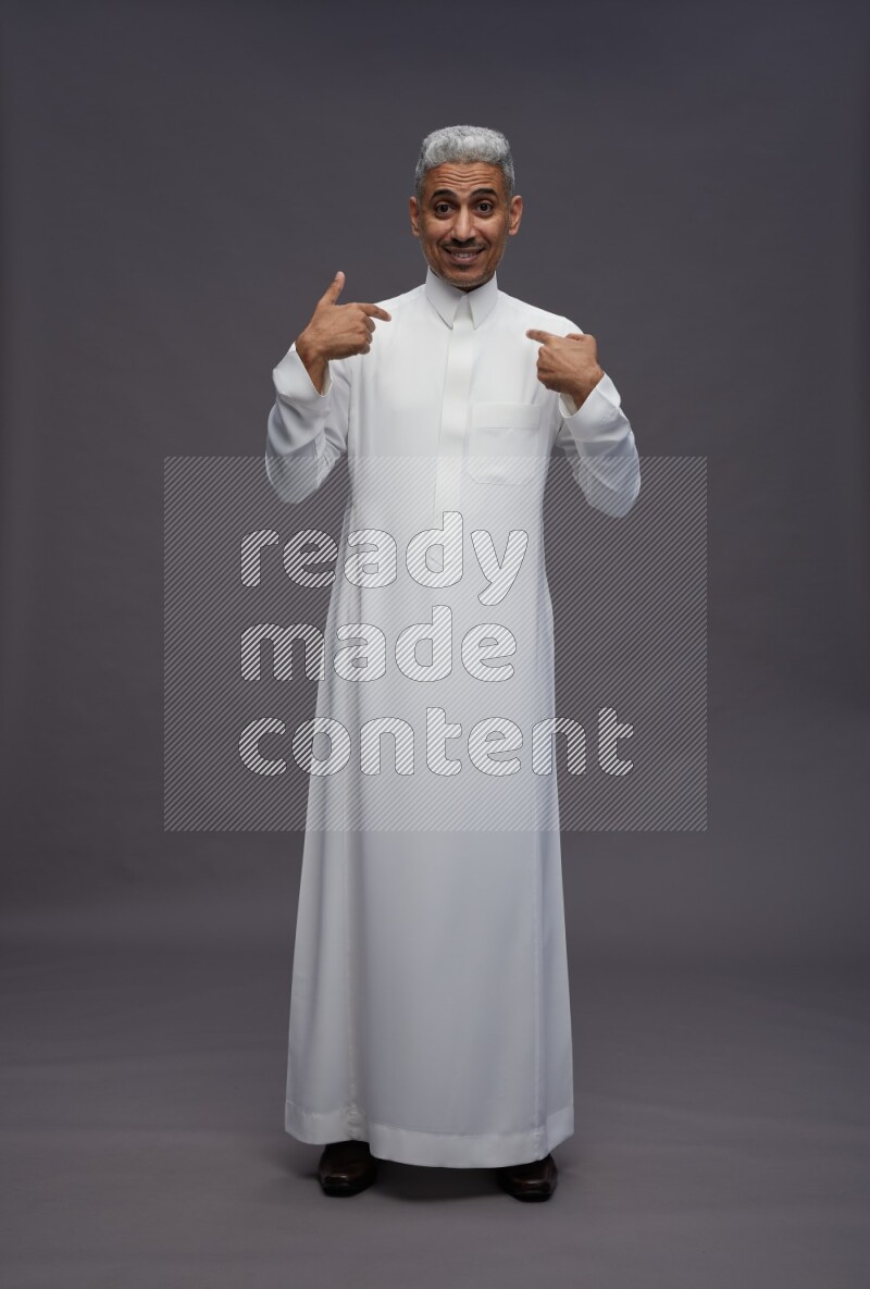 Saudi man wearing thob standing interacting with the camera on gray background