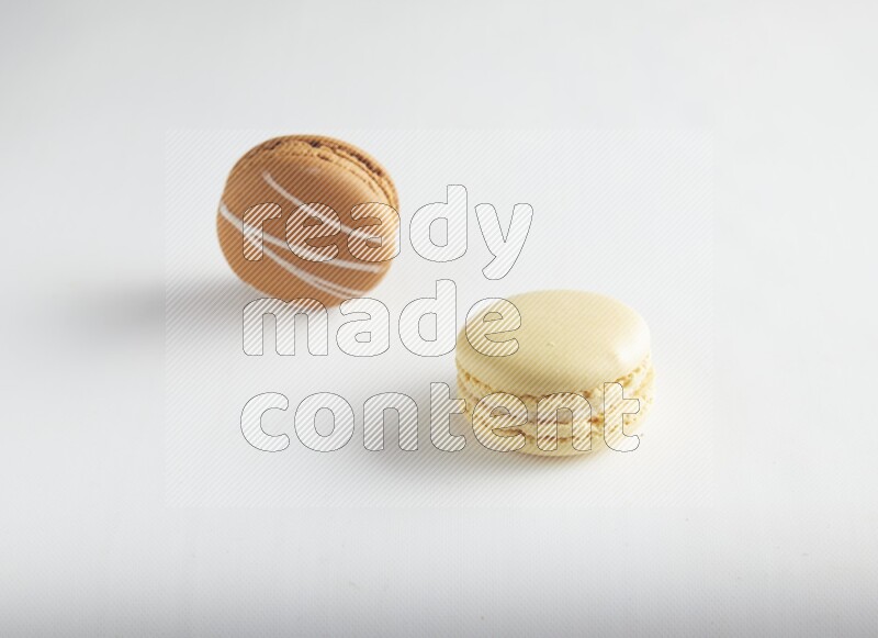 45º Shot of of two assorted Brown Irish Cream, and Yellow Vanilla macarons on white background