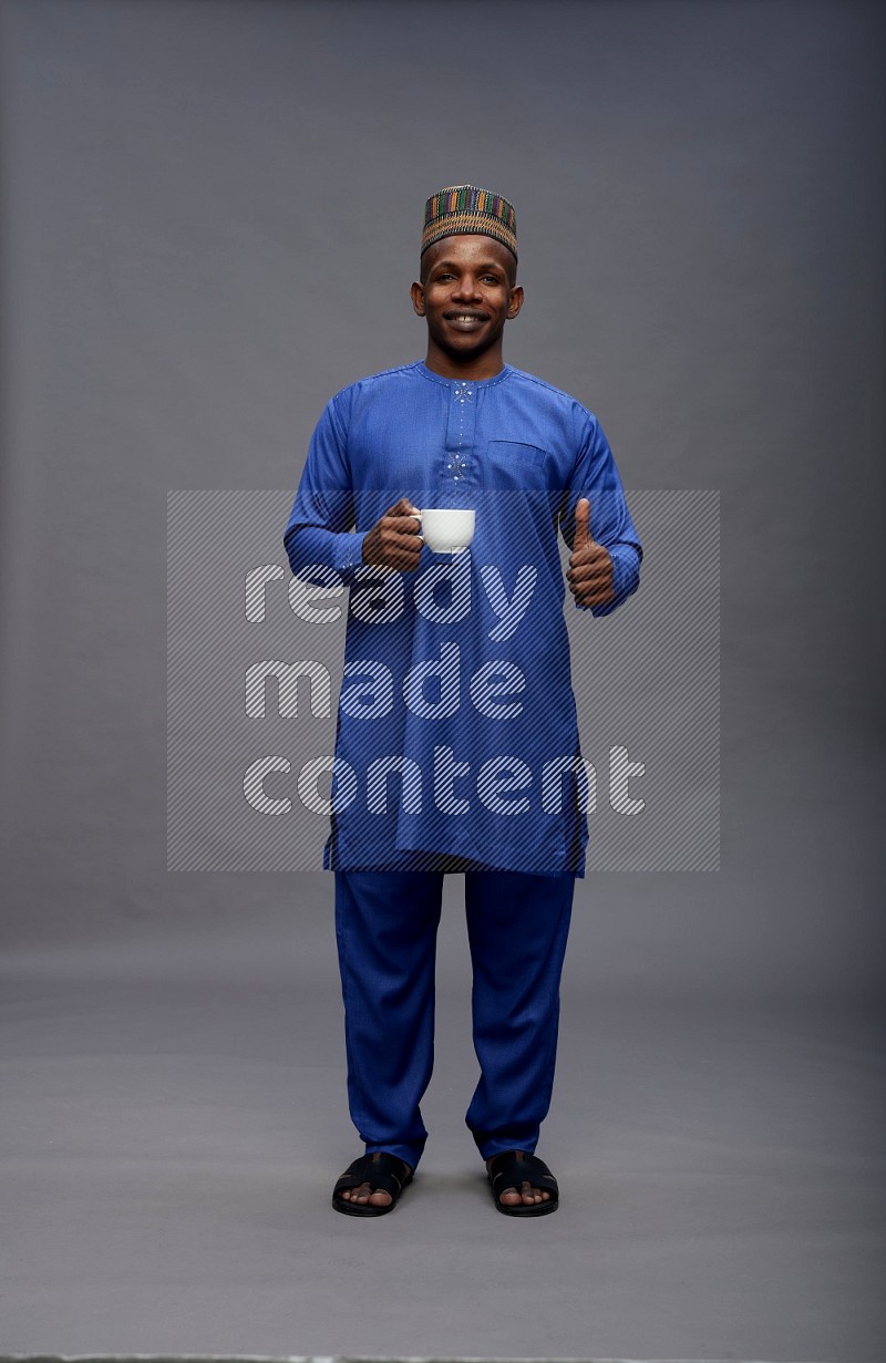 Man wearing Nigerian outfit standing holding mug on gray background