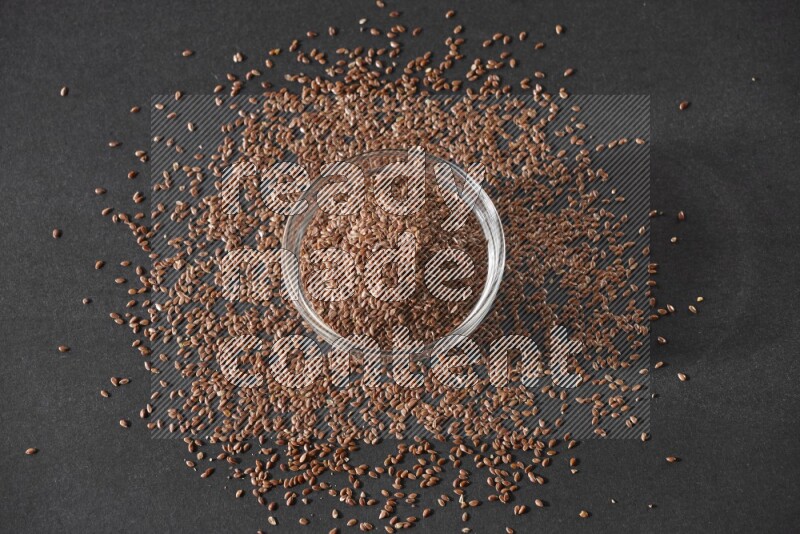 وعاء زجاجي ممتلئ بحبوب بذر الكتان محاط بالبذور على أرضية سوداء