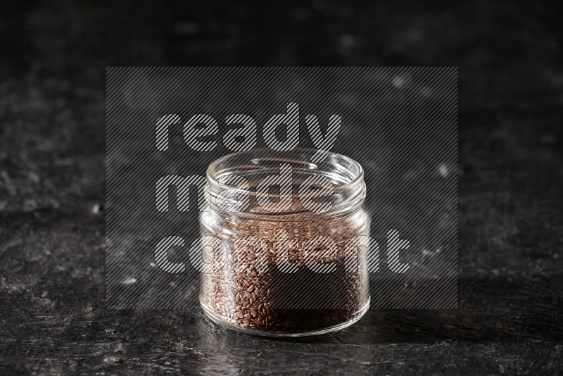A glass jar full of flaxseeds on a textured black flooring