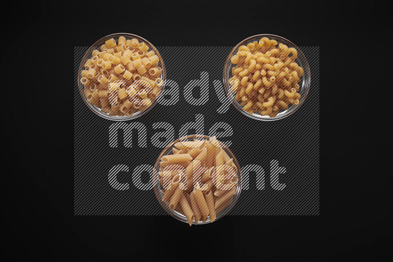 Different pasta types in glass bowls on black background