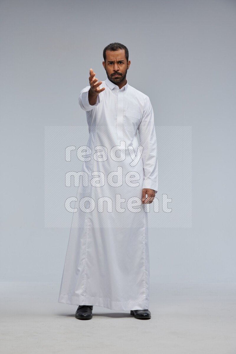 Saudi man Wearing Thob standing interacting with the camera on Gray background
