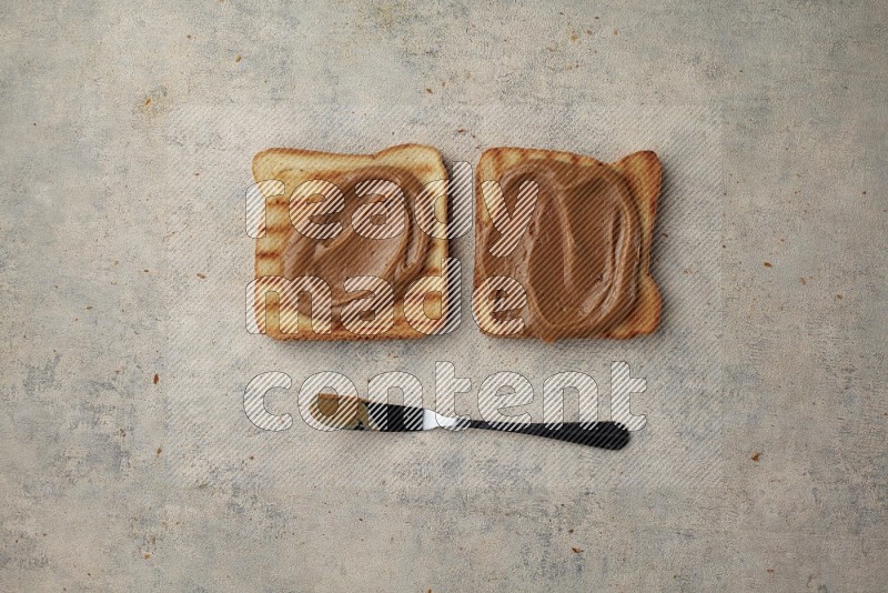Creamy peanut butter on a toasted white toast slices with a spreading knife on a light blue textured background