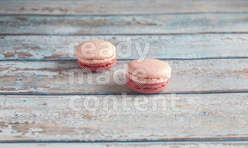 45º Shot of two Pink Litchi Raspberry macarons on light blue wooden background