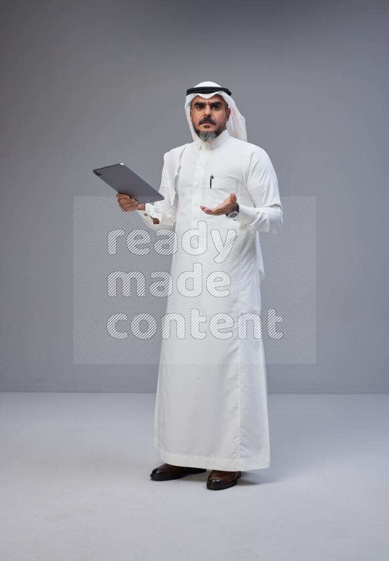 Saudi man Wearing Thob and white Shomag standing working on tablet on Gray background