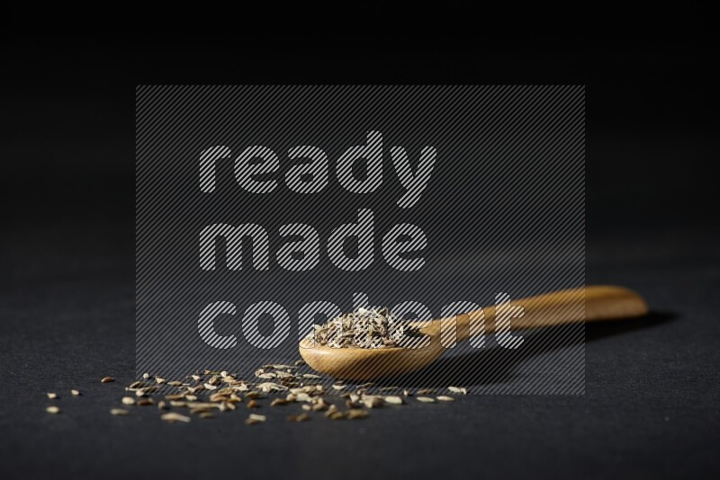 ملعقة خشبية ممتلئة بحبوب الكمون على خلفية سوداء