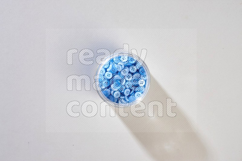 A glass jar full of colored buttons on grey background