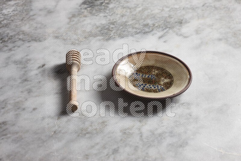 Decorative pottery plate with wooden honey dipper on the side on grey marble background