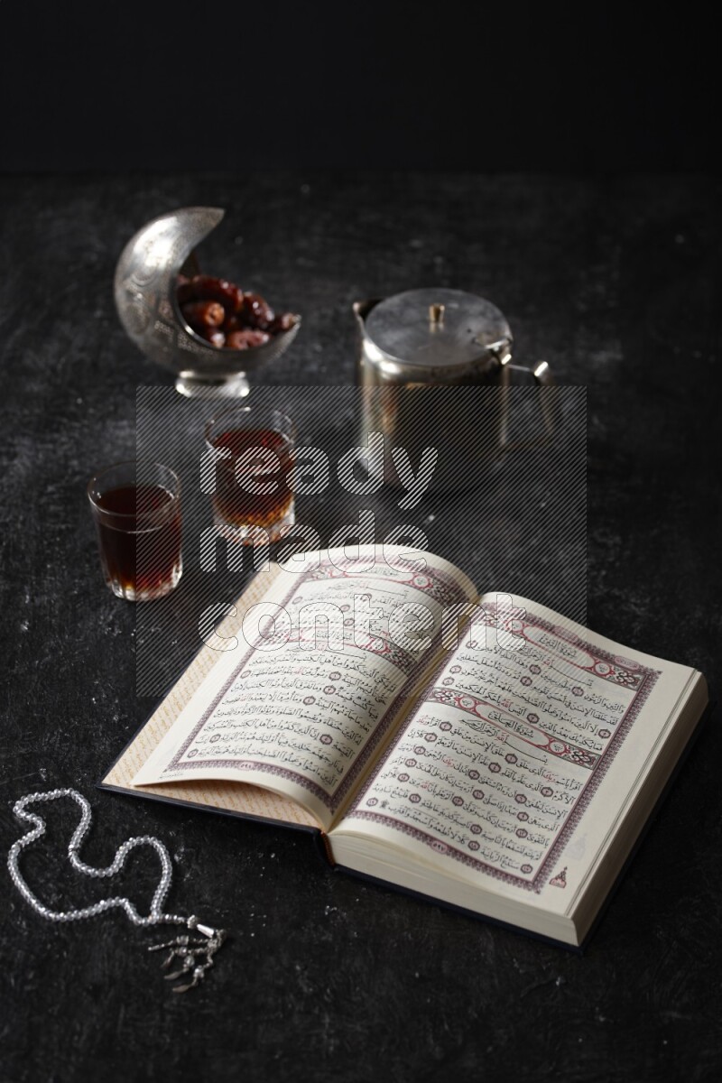 Moshaf with tea cups and prayer beads in a dark setup