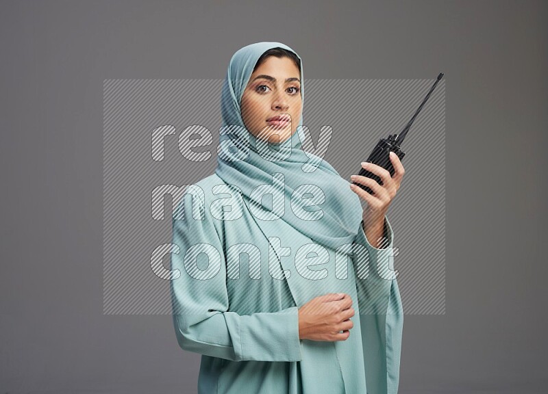 Saudi Woman wearing Abaya standing holding walkie-talkie on Gray background