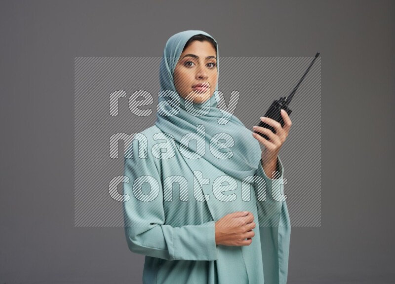 Saudi Woman wearing Abaya standing holding walkie-talkie on Gray background