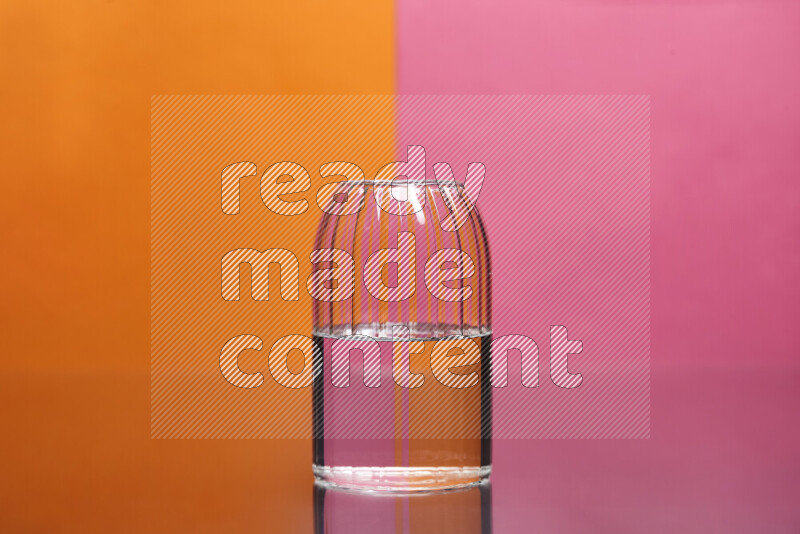The image features a clear glassware filled with water, set against orange and pink background