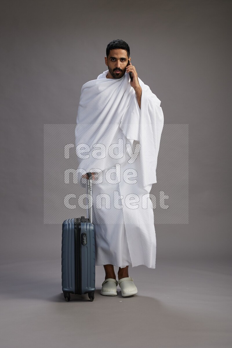 A man wearing Ehram Standing holding traveling bag on gray background