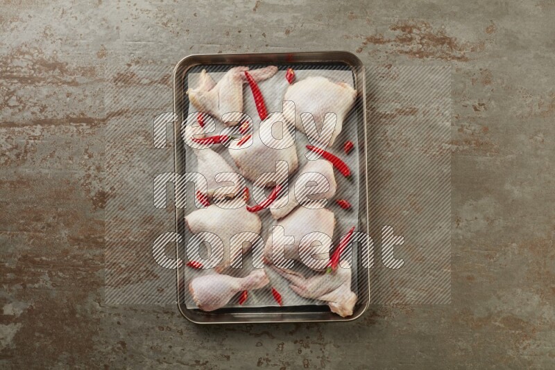 Mixed fresh chicken pieces in an oven tray on a textured rustic background
