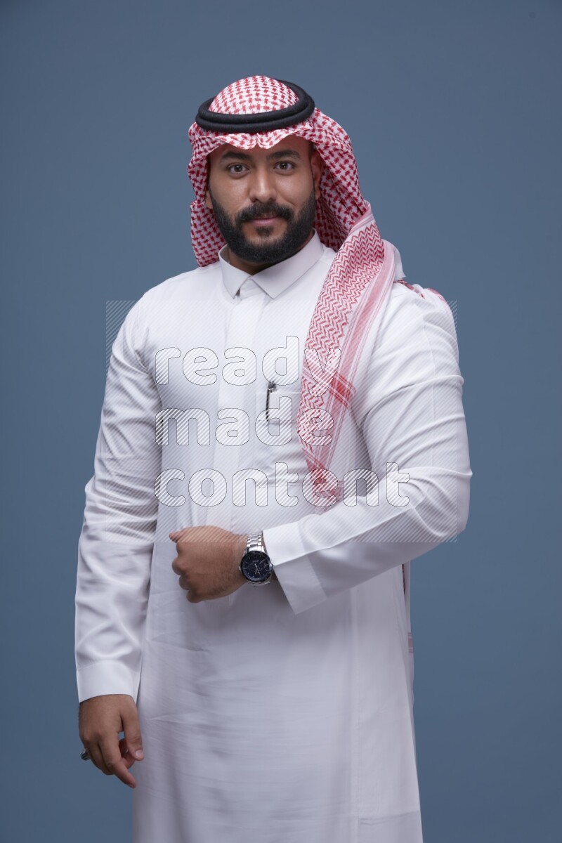 A Saudi man posing on blue background wearing Thob and Shomag