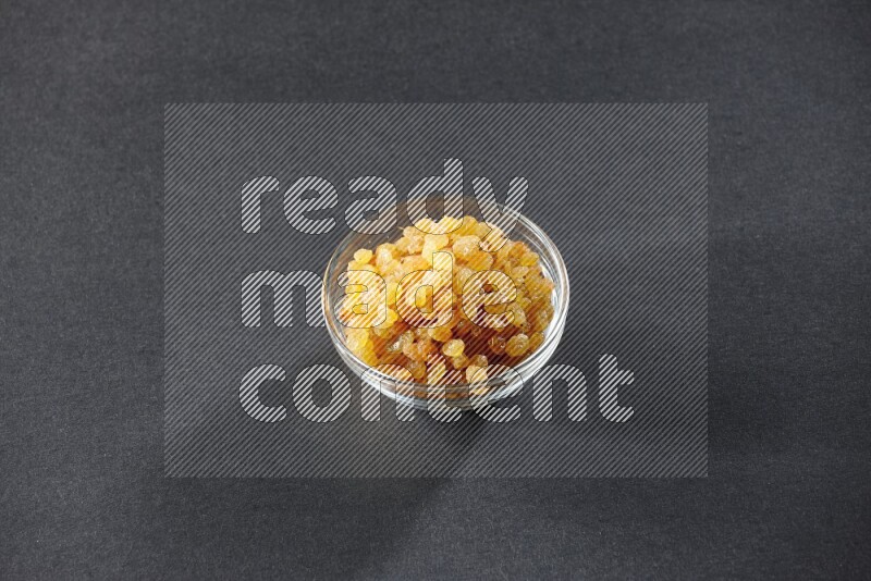 A glass bowl full of raisins on a black background in different angles