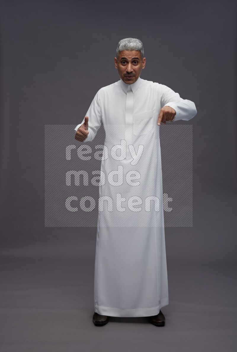Saudi man wearing thob standing interacting with the camera on gray background