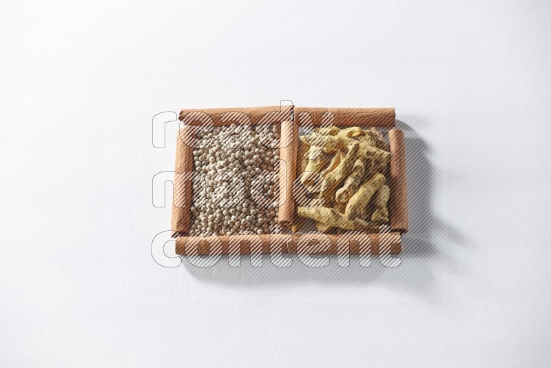 مربعان من أعواد القرفة ممتلئان بحبوب الفلفل الأبيض وأصابع الكركم علي خلفية بيضاء