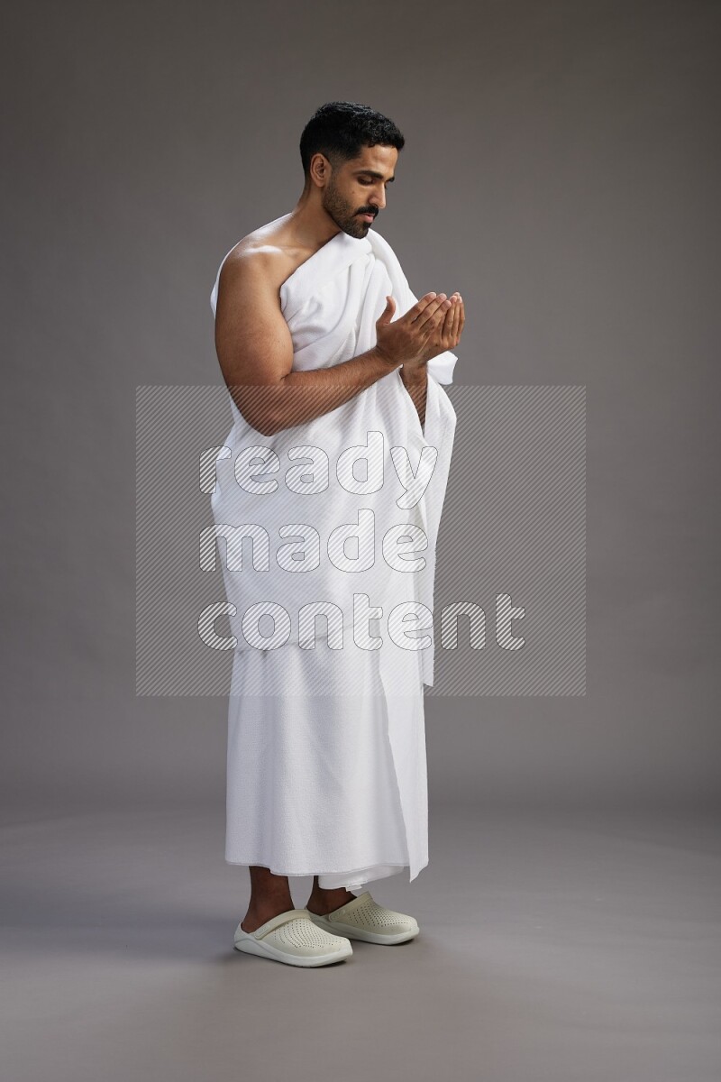 A man wearing Ehram Standing performing dua'a on gray background