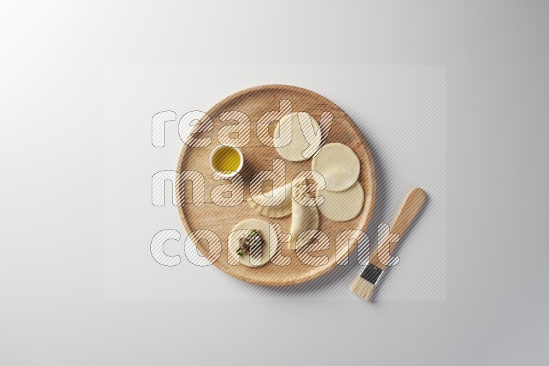 two closed sambosas and one open sambosa filled with meat while oil with oil brush aside in a wooden dish on a white background