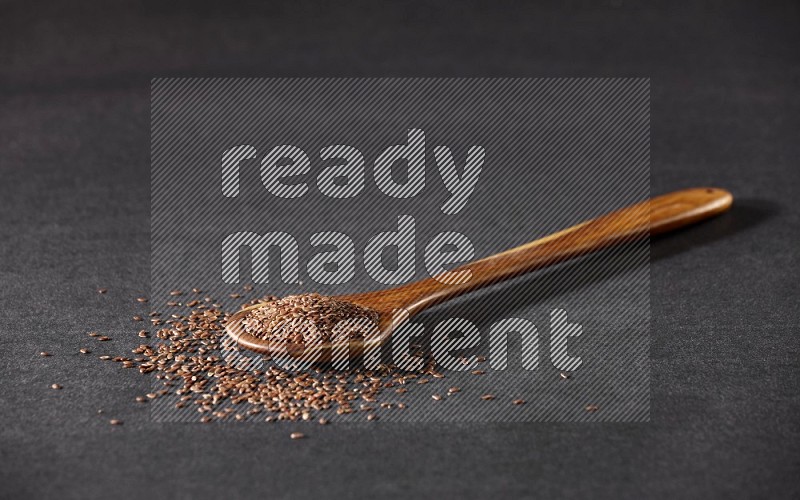 A wooden ladle full of flax and seeds spreaded beside it on a black flooring in different angles
