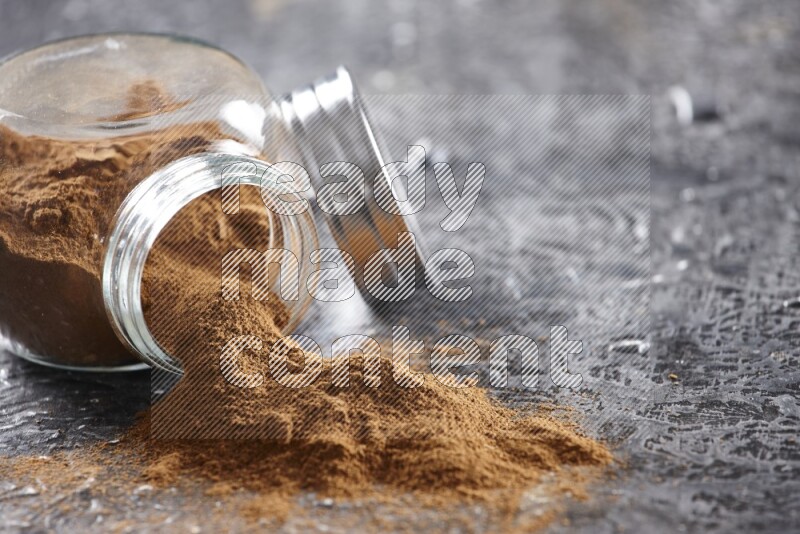 Flipped herbal glass jar full of cinnamon powder on textured black background