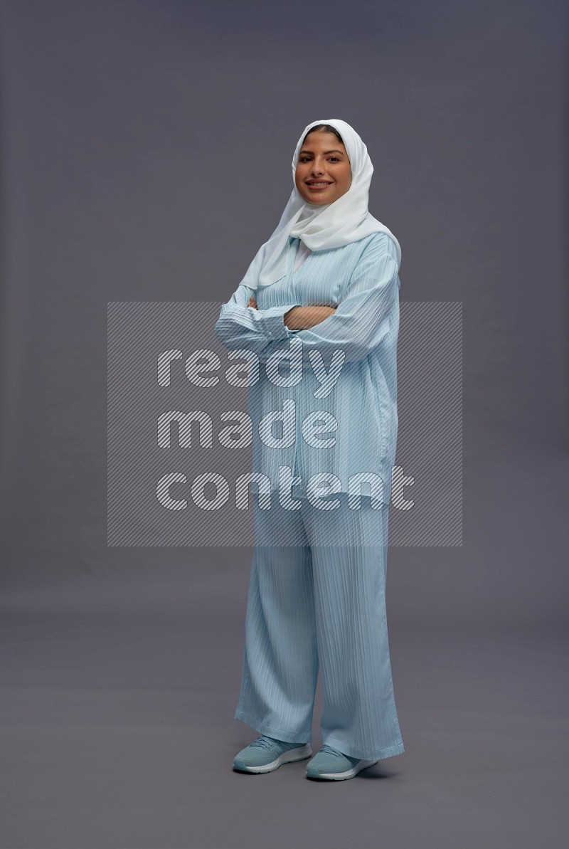 Saudi woman wearing hijab clothes standing with crossed arms on gray background
