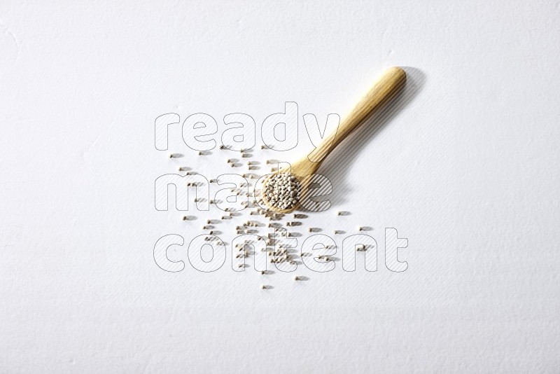 A wooden spoon full of white pepper beads on white flooring